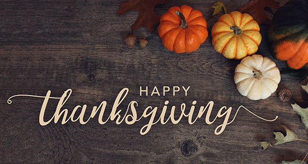 Rustic Thanksgiving image with "Happy Thanksgiving" text in elegant script on a wooden background, surrounded by small pumpkins and autumn leaves.